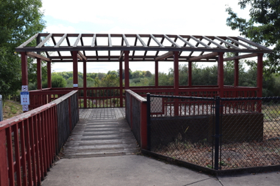 Overlook of wetlands – fence on sides of walkway – north view parking lot – paved to wooden surface